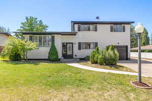 View of front of house with brick siding, concrete driveway, an attached garage, a front lawn, and a chimney