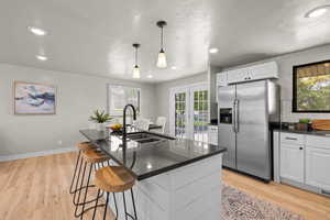 Kitchen with stainless steel fridge with ice dispenser, white cabinets, plenty of natural light, light wood-type flooring, and recessed lighting