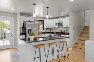 Kitchen with appliances with stainless steel finishes, a breakfast bar, backsplash, white cabinetry, and light wood finished floors