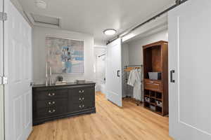 Bedroom featuring a barn door, light wood-style flooring, attic access, and ensuite bath