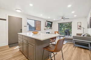 Kitchen with open floor plan, light wood-style floors, a breakfast bar area, a ceiling fan, and a kitchen island