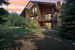 Rear view of house featuring a balcony, a chimney, and a lawn