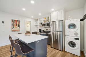 Kitchen with stainless steel appliances, stacked washer and clothes dryer, open shelves, a center island, and white cabinets