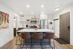 Kitchen featuring appliances with stainless steel finishes, stacked washer and clothes dryer, open shelves, a breakfast bar area, and tasteful backsplash