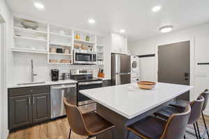 Kitchen featuring stainless steel appliances, stacked washing machine and dryer, open shelves, a kitchen bar, and light wood finished floors