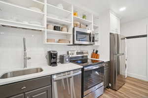 Kitchen featuring appliances with stainless steel finishes, open shelves, decorative backsplash, light wood-style flooring, and white cabinetry