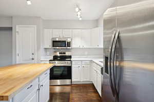 Kitchen featuring stainless steel appliances, butcher block counters, white cabinets, and dark wood-style flooring