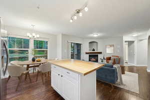 Kitchen with butcher block counters, white cabinets, open floor plan, a warm lit fireplace, and dark wood-type flooring