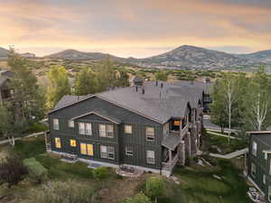 Back of property at dusk with a shingled roof, board and batten siding, a mountain view, and a balcony