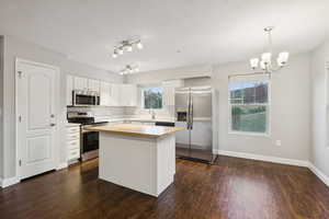 Kitchen with stainless steel appliances, dark wood-style floors, a chandelier, butcher block countertops, and white cabinets