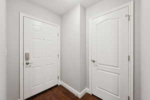 Doorway to outside with dark wood-type flooring and baseboards