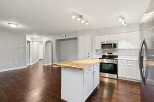 Kitchen featuring stainless steel appliances, wooden counters, white cabinets, a center island, and dark wood finished floors