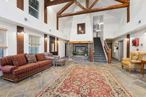 Living room featuring high vaulted ceiling, stone tile flooring, stairway, a fireplace, and beamed ceiling
