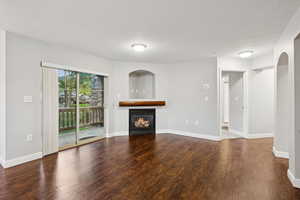 Unfurnished living room with wood finished floors, a glass covered fireplace, and a textured ceiling