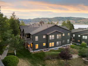 Back of property at dusk with roof with shingles, board and batten siding, a mountain view, and a lawn