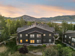 Back of property at dusk featuring board and batten siding, a water and mountain view, and a shingled roof