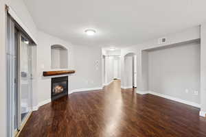 Unfurnished living room featuring wood finished floors, a glass covered fireplace, and arched walkways