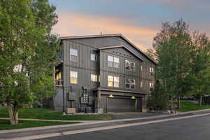 View of front facade featuring an attached garage, asphalt driveway, board and batten siding, and a front yard