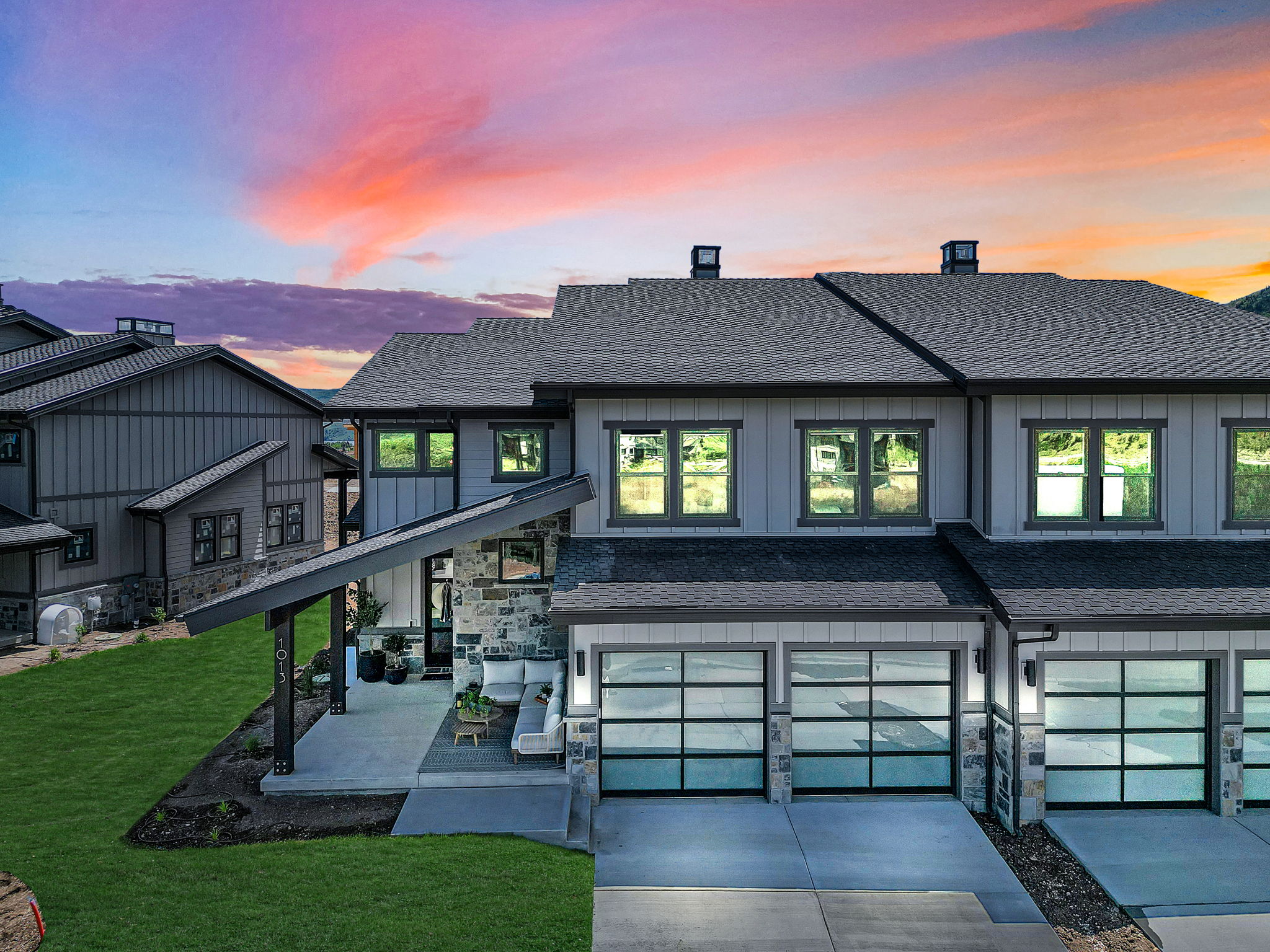View of front of property featuring an attached garage, concrete driveway, stone siding, roof with shingles, and board and batten siding
