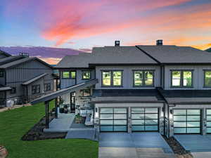 View of front of property featuring an attached garage, concrete driveway, stone siding, roof with shingles, and board and batten siding