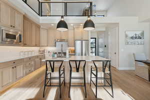 Kitchen with appliances with stainless steel finishes, light brown cabinetry, a high ceiling, under cabinet range hood, and light wood-style flooring