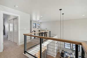 Hall with an upstairs landing, light colored carpet, and recessed lighting