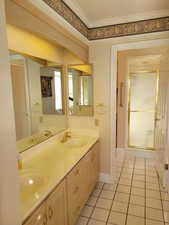 Bathroom with tile patterned flooring, double vanity, ornamental molding, and a shower with door