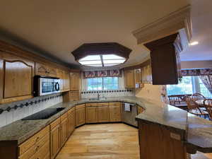 Kitchen with stainless steel appliances, a peninsula, light wood-style flooring, decorative backsplash, and crown molding