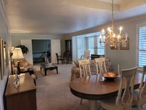 Carpeted dining area featuring a chandelier and ornamental molding