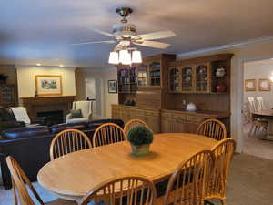 Dining space featuring light carpet, crown molding, a ceiling fan, and a tiled fireplace