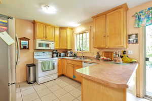 Kitchen featuring white appliances, a peninsula, light brown cabinetry, light tile patterned floors, and light countertops