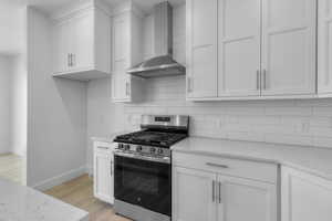 Kitchen featuring stainless steel gas stove, wall chimney range hood, light wood-style floors, white cabinetry, and tasteful backsplash