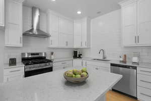 Kitchen featuring appliances with stainless steel finishes, wall chimney range hood, decorative backsplash, white cabinetry, and recessed lighting