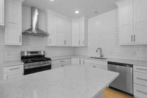 Kitchen with stainless steel appliances, wall chimney exhaust hood, tasteful backsplash, white cabinets, and recessed lighting
