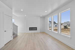 Living room with light wood finished floors, stairway, recessed lighting, and a large fireplace