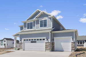 View of front of house featuring stone siding, driveway, an attached garage, and a shingled roof