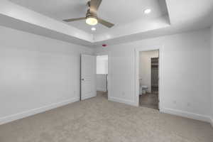 Primary bedroom featuring light carpet, a raised ceiling, recessed lighting, a walk in closet, and a ceiling fan