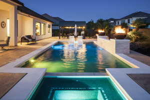 Pool at night with a fire pit, a patio, and a pool with connected hot tub