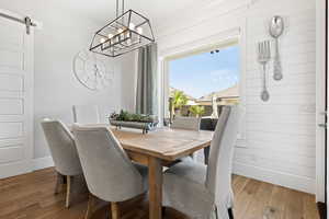 Dining area with wood finished floors, a chandelier, and a barn door
