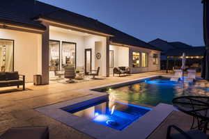 Pool at night featuring a patio, a pool with connected hot tub, and outdoor lounge area