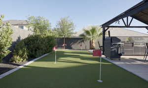 Fenced backyard featuring a putting area and exterior kitchen