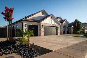 View of front of home featuring a garage, a tile roof, board and batten siding, driveway, and stone siding