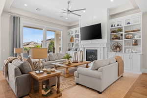 Living area featuring a ceiling fan, light wood-style flooring, a glass covered fireplace, built in features, and recessed lighting