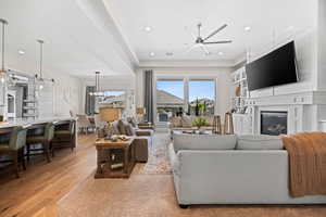 Living room with light wood-style flooring, ceiling fan, a glass covered fireplace, recessed lighting, and a chandelier
