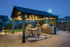 Patio at twilight featuring exterior kitchen, a gazebo, a patio area, and a fenced backyard