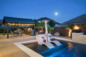 Fenced backyard with a gazebo, an outdoor kitchen, an outdoor fire pit, a patio area, and outdoor dining space