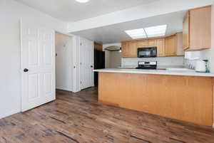 Kitchen featuring a peninsula, dark wood-type flooring, light countertops, black appliances, and light brown cabinets