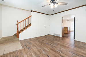 Unfurnished living room featuring ornamental molding, a ceiling fan, dark wood finished floors, arched walkways, and stairs