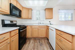 Kitchen featuring black appliances, light wood-style flooring, light countertops, a peninsula, and light brown cabinets