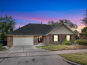 Ranch-style house with concrete driveway, brick siding, an attached garage, a chimney, and roof with shingles